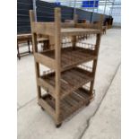 A TALL RUSTIC FOUR TIER WOODEN FOUR WHEELED STAND WITH WIRE BASKET TRAYS