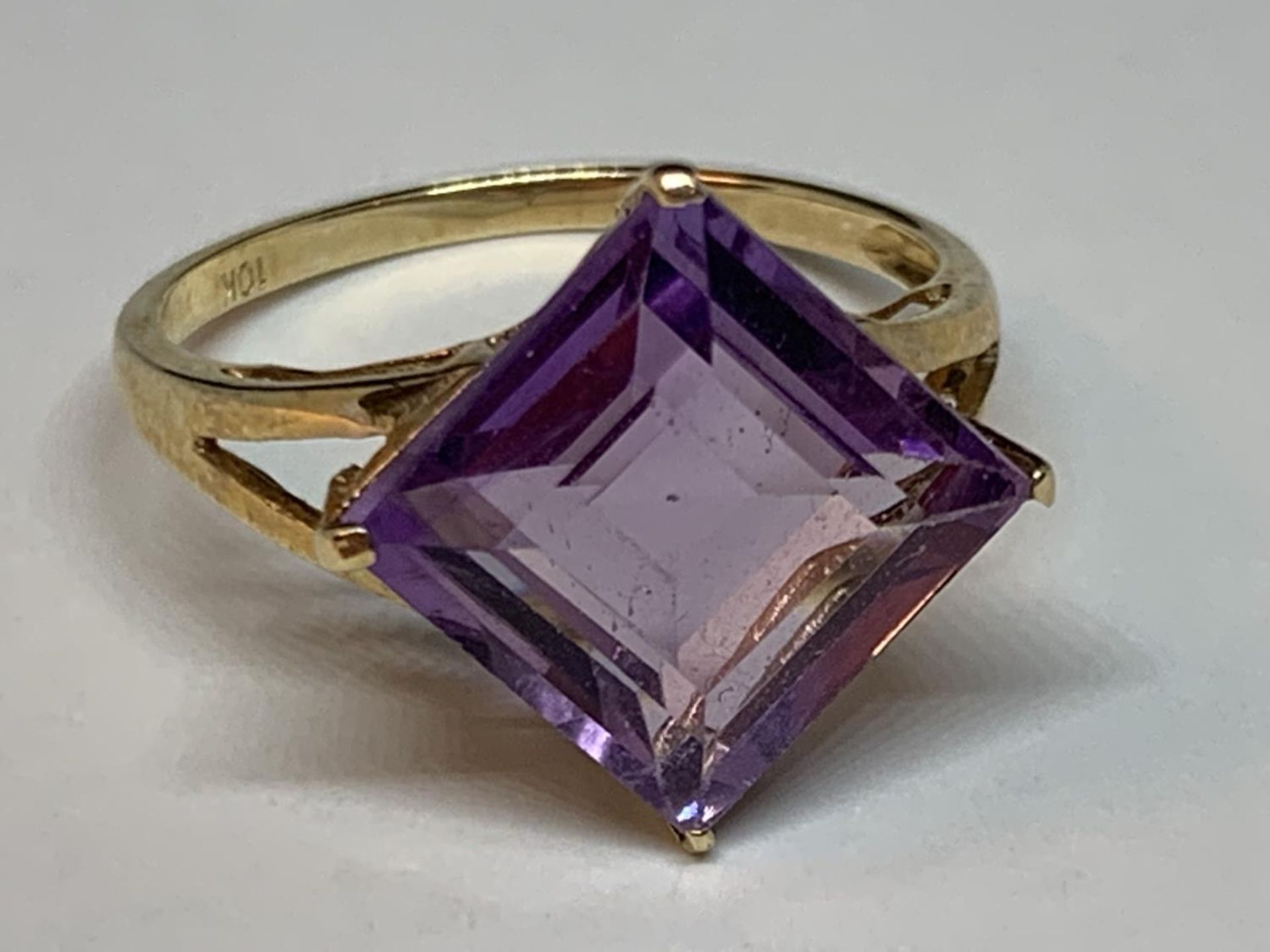 A 10 CARAT GOLD RING WITH A PURPLE DIAMOND SHAPED STONE SIZE O