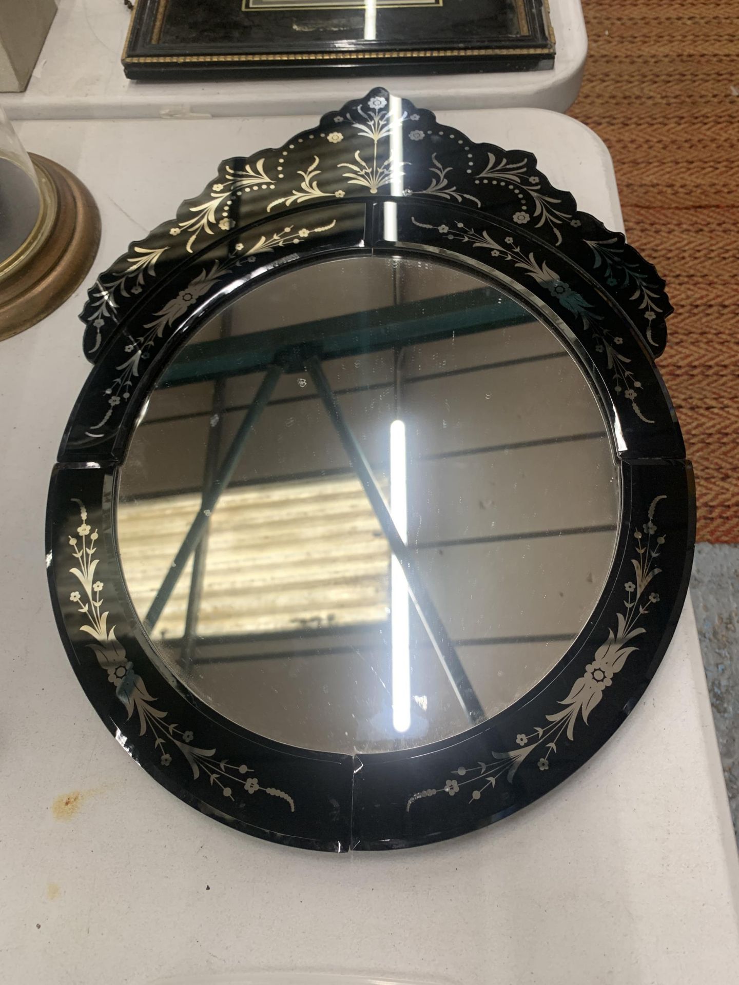 A BLACK GLASS MIRROR WITH AN ORNATE TOP