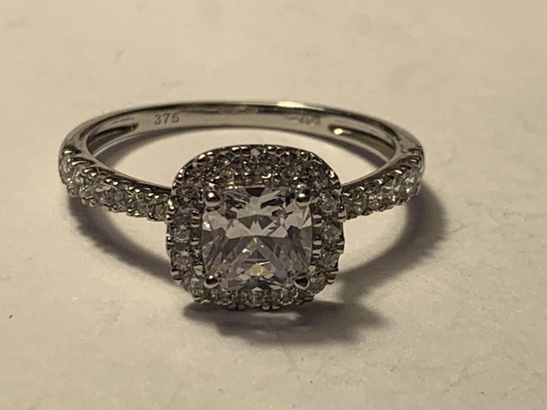 A 9 CARAT WHITE GOLD RING WITH A LARGE SQUARE CUBIC ZIRCONIA ALSO SURROUNDED AND ON THE SHOULDERS