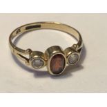 A 9 CARAT GOLD RING WITH A RED GARNET AND A CUBIC ZIRCONIA EACH SIDE SIZE N/O