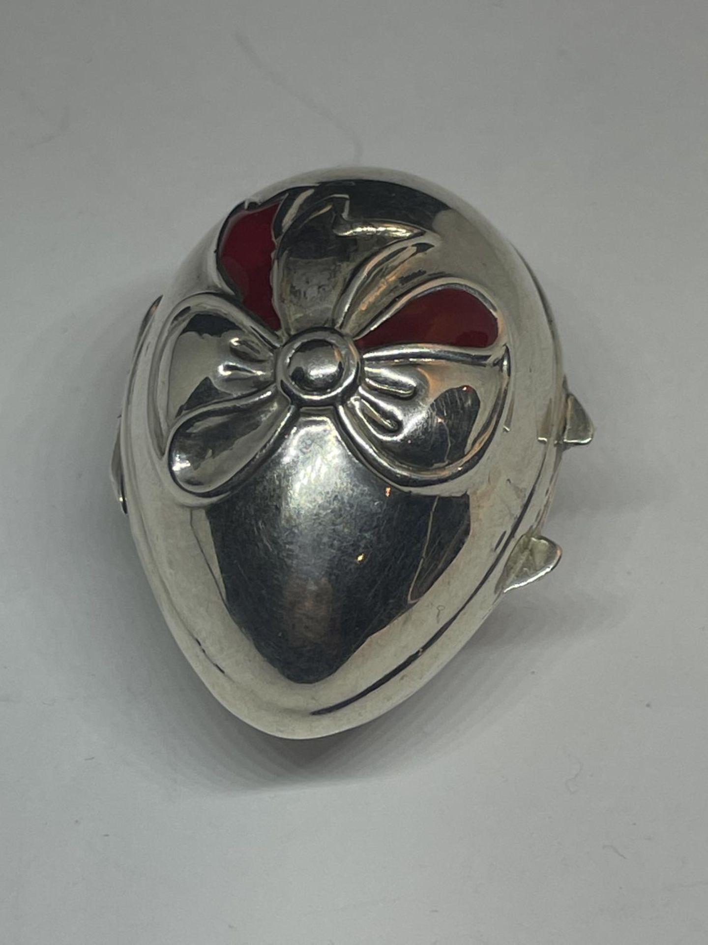 A SILVER EGG SHAPED PILL BOX WITH RIBBON DESIGN ON THE LID