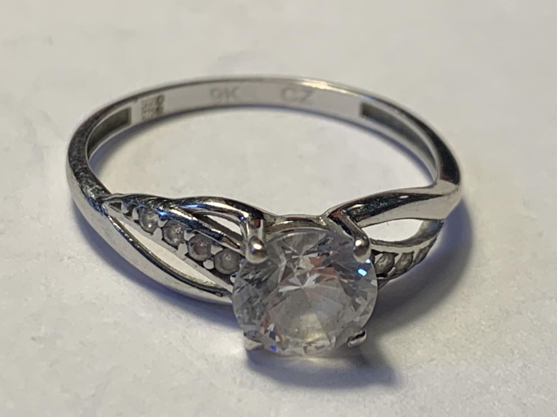 A 9 CARAT WHITE GOLD RING WITH A WITH A LARGE CENTRE CUBIC ZIRCONIA AND SMALLER TO THE SHOULDERS