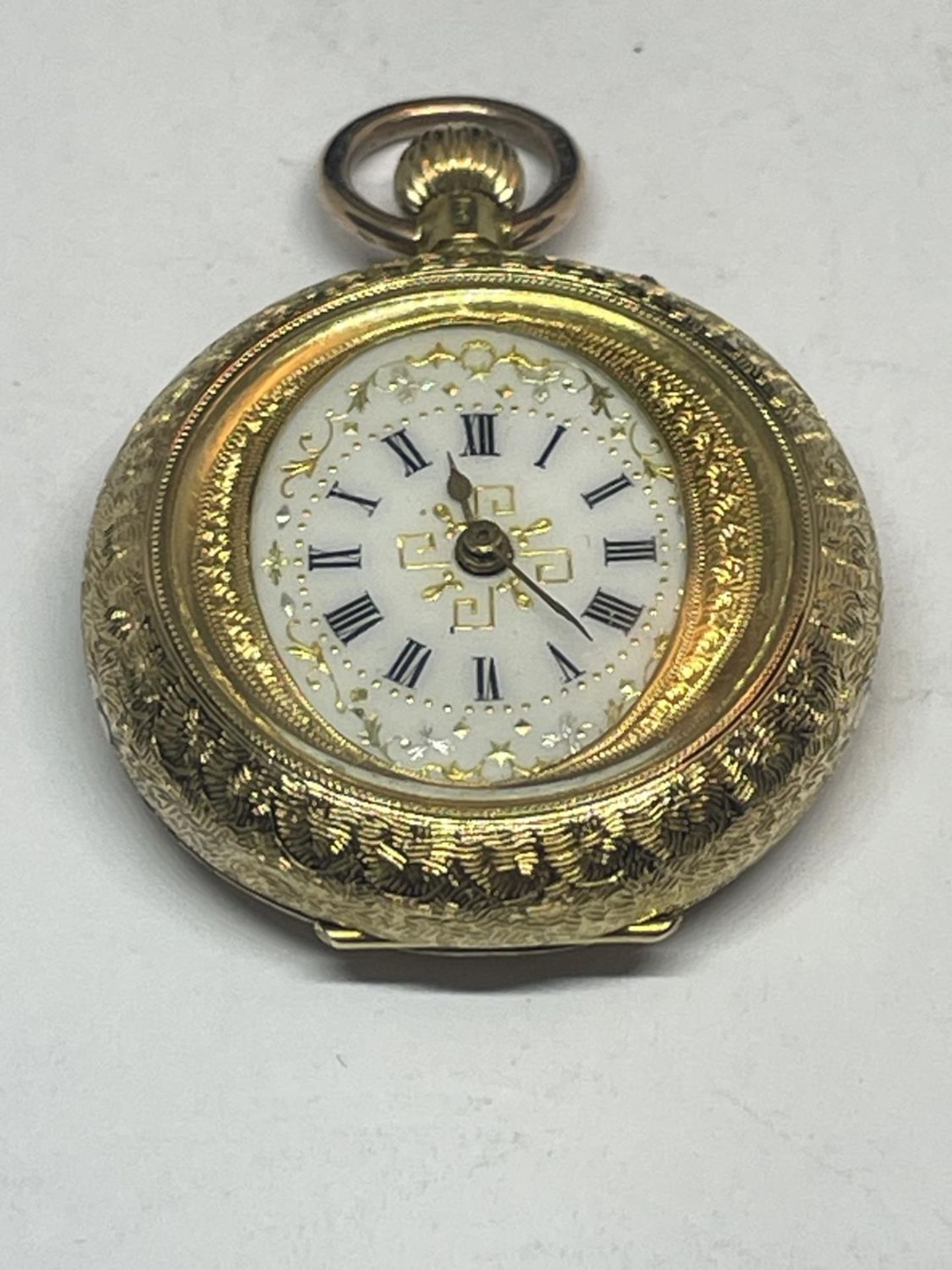 AN ORNATE 18 CARAT GOLD FOB WATCH WITH WHITE ENAMAL FACE AND ROMAN NUMERALS WITH FLOWER DESIGN TO