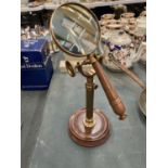 A BRASS MAGNIFYING GLASS ON A GLASS STAND AND WOODEN BASE