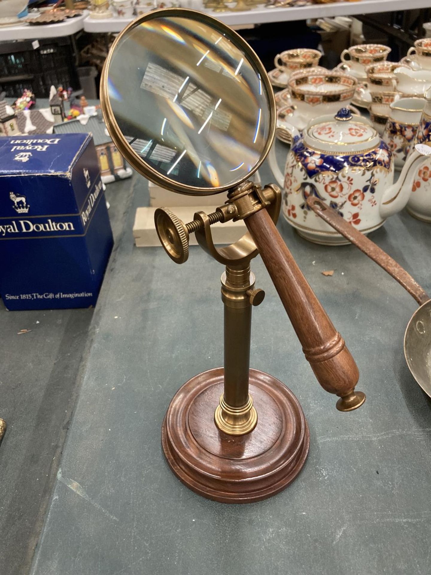 A BRASS MAGNIFYING GLASS ON A GLASS STAND AND WOODEN BASE