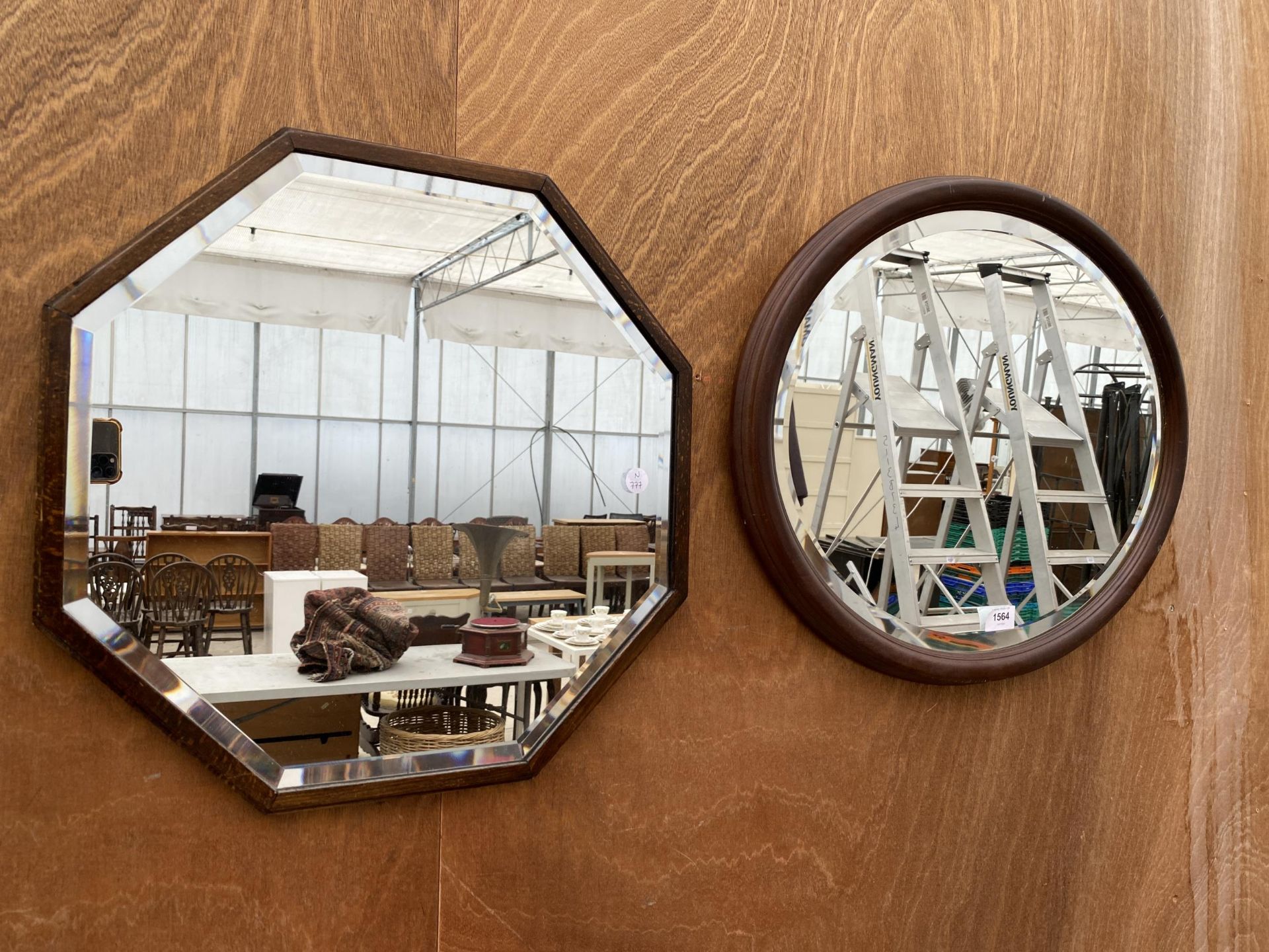 AN OVAL OAK FRAMED BEVELED EDGE WALL MIRROR AND A FURTHER OCTAGONAL OAK FRAMED BEVELED EDGE WALL