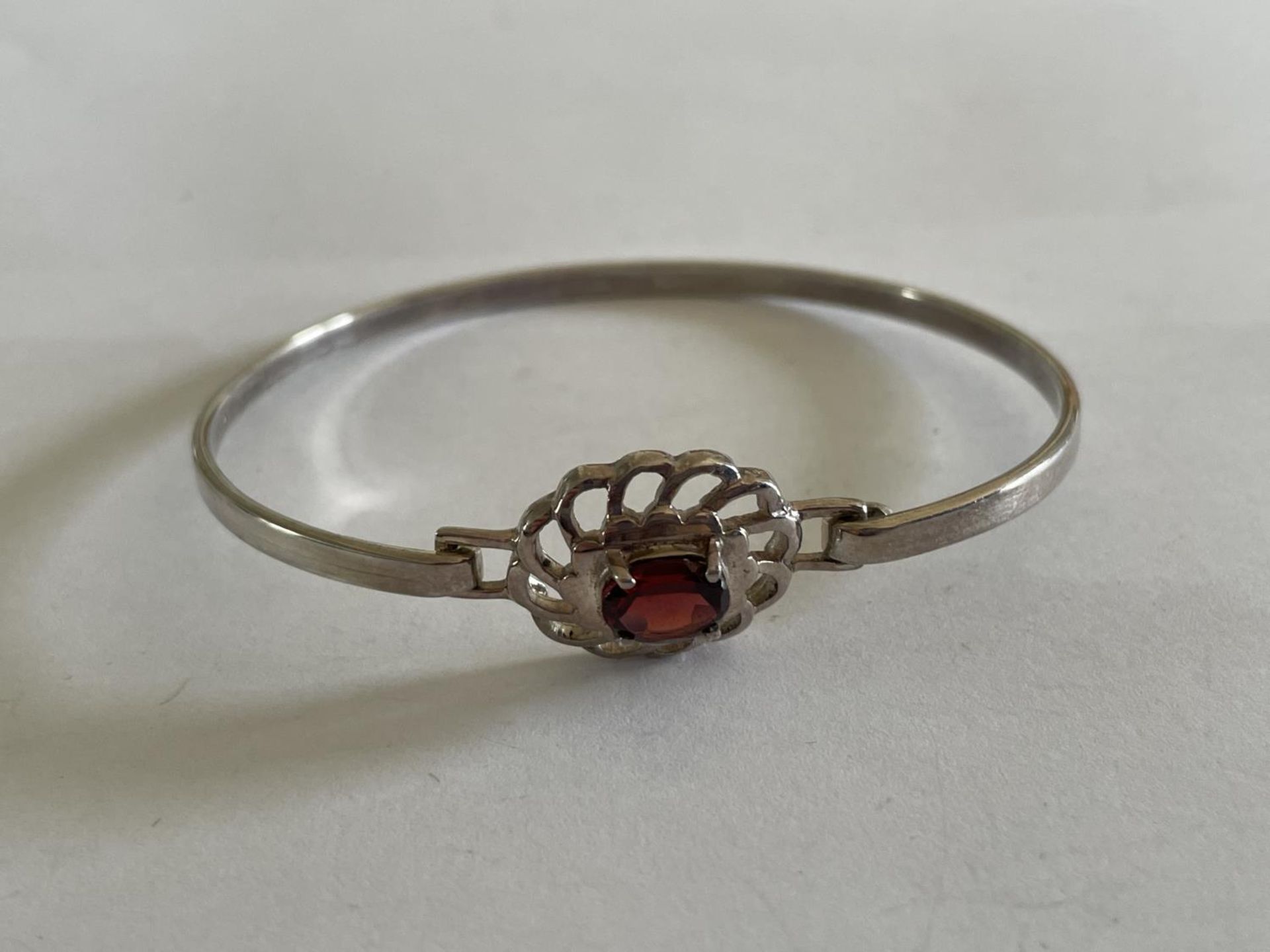 A SILVER BANGLE WITH RED STONE