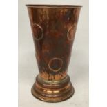 A VINTAGE COPPER GAMBLING TAVERN DICE SHAKING BEAKER EMBEDDED WITH COINS AND DICE BENEATH A GLASS