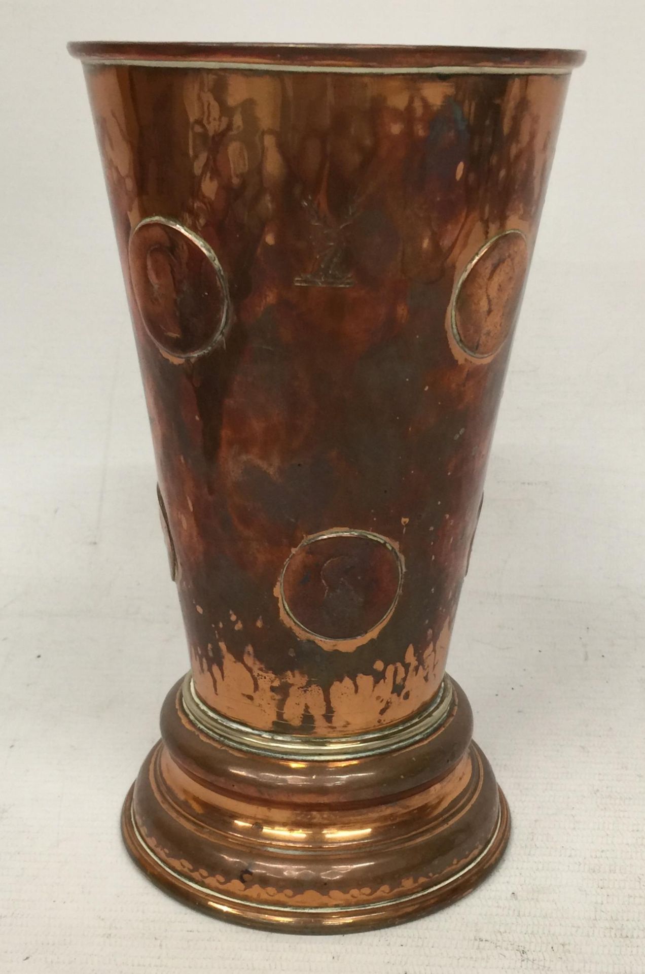 A VINTAGE COPPER GAMBLING TAVERN DICE SHAKING BEAKER EMBEDDED WITH COINS AND DICE BENEATH A GLASS