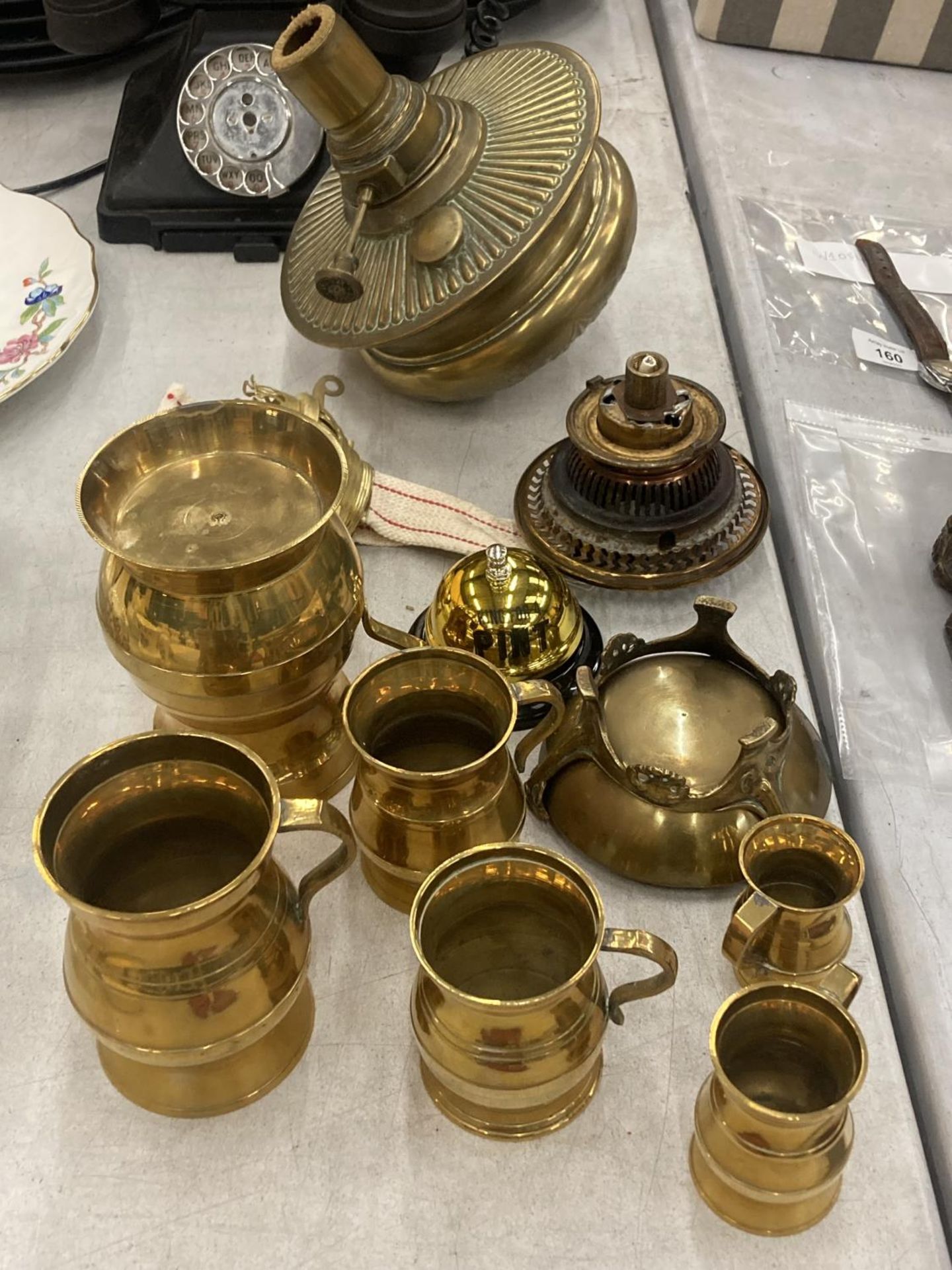 A QUANTITY OF BRASSWARE TO INCLUDE TANKARDS OF VARYING SIZES, A COUNTER BELL, OIL LAMP PARTS, ETC