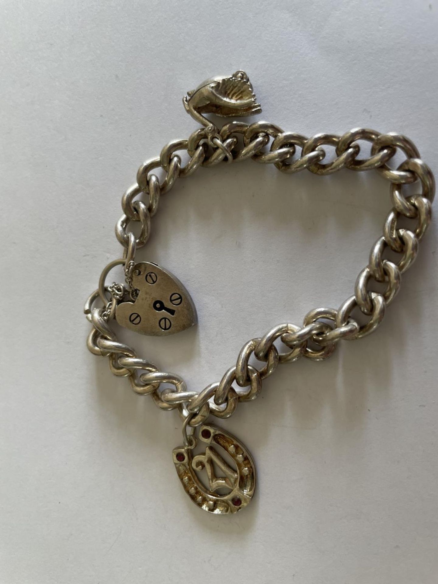 A HEAVY SILVER BRACELET WITH TWO CHARMS AND A HEART SHAPED PADLOCK