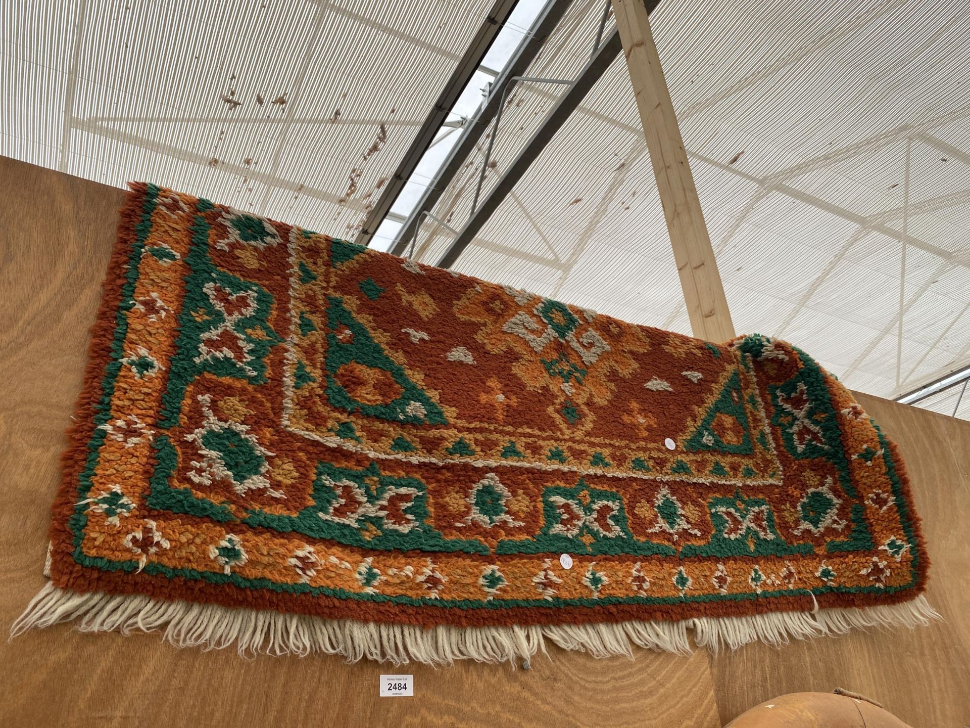 AN ORANGE AND GREEN PATTERNED FRINGED RUG