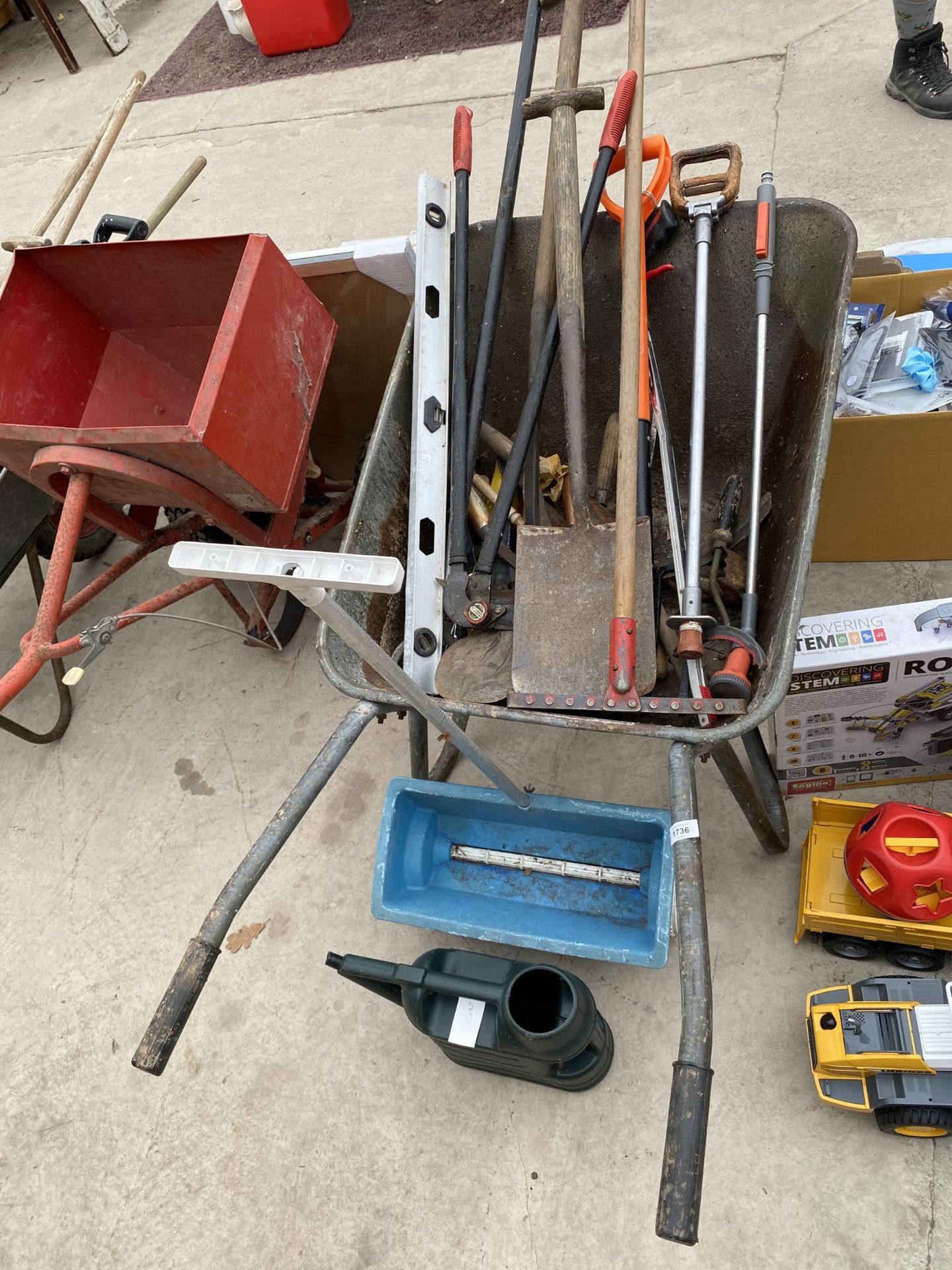 A METAL WHEEL BARROW AND AN ASSORTMENT OF GARDEN TOOLS TO INCLUDE A SEEDER AND SPADES ETC