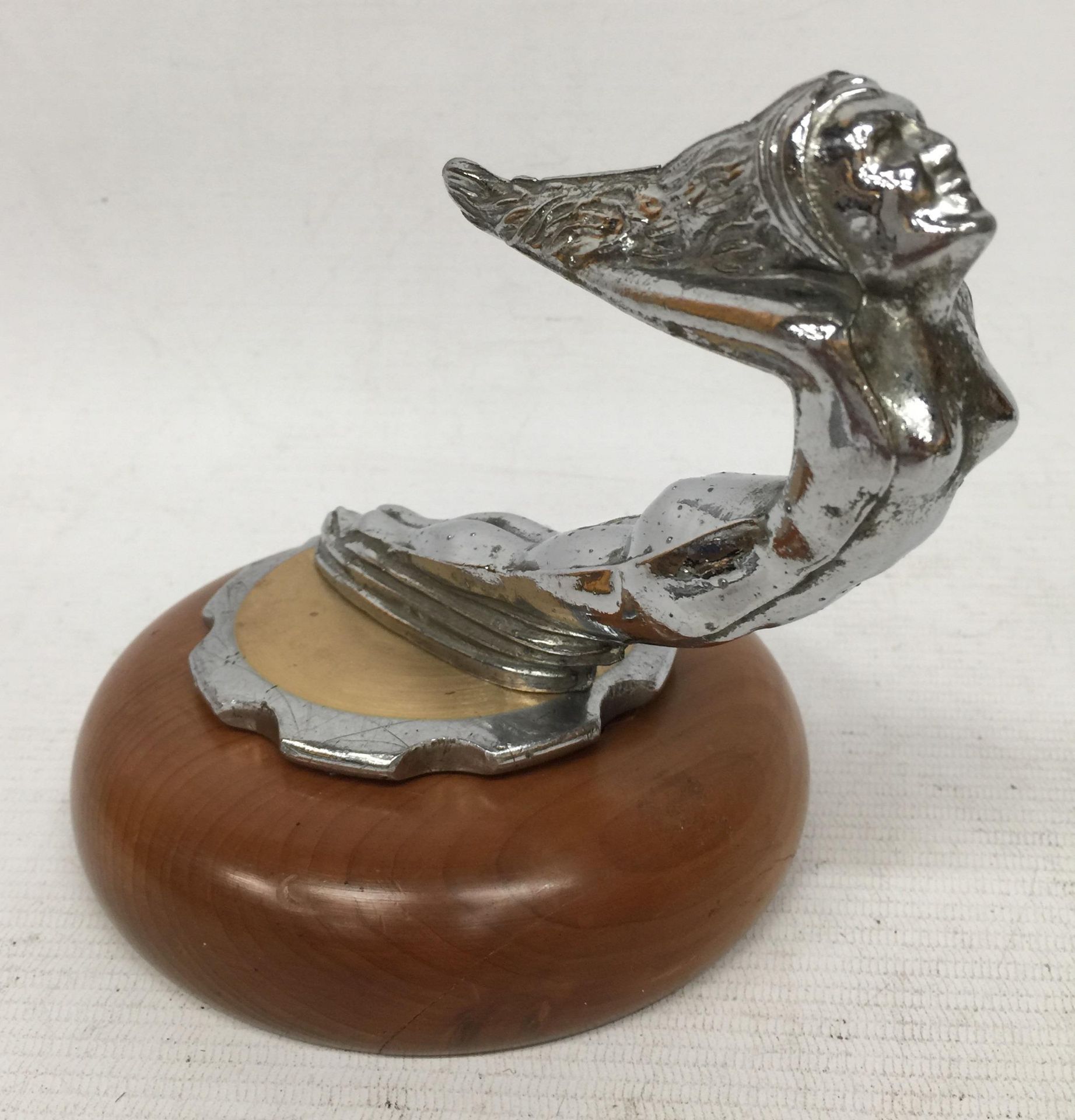 A NUDE LADY CHROME EFFECT CAR MASCOT ON WOODEN BASE