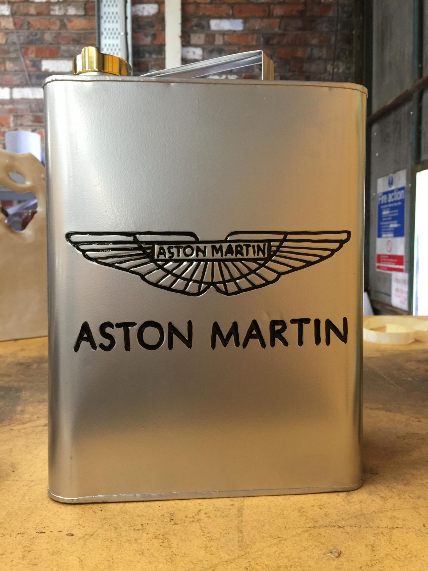 A SILVER COLOURED METAL ASTON MARTIN PETROL CAN WITH BRASS TOP