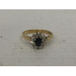 AN 18CT RING WITH CENTRE DARK STONE (POSSIBLY SAPPHIRE) SURROUNDED BY DIAMOND CHIPS