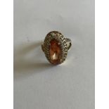A DECORATIVE SILVER AND GOLD RING WITH LARGE AMBER COLOURED STONE SURROUNDED BY CLEAR STONES SIZE