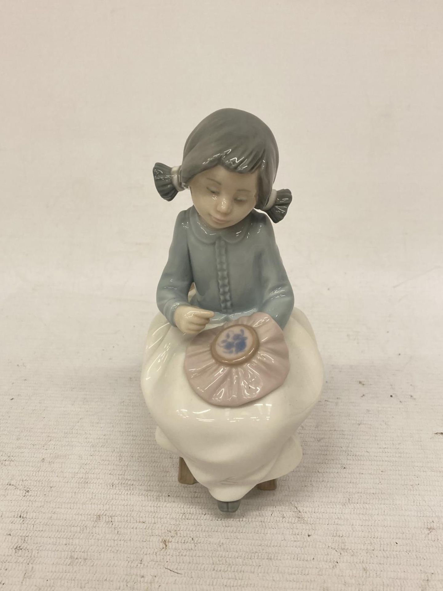 A NAO FIGURINE OF A GIRL SEWING