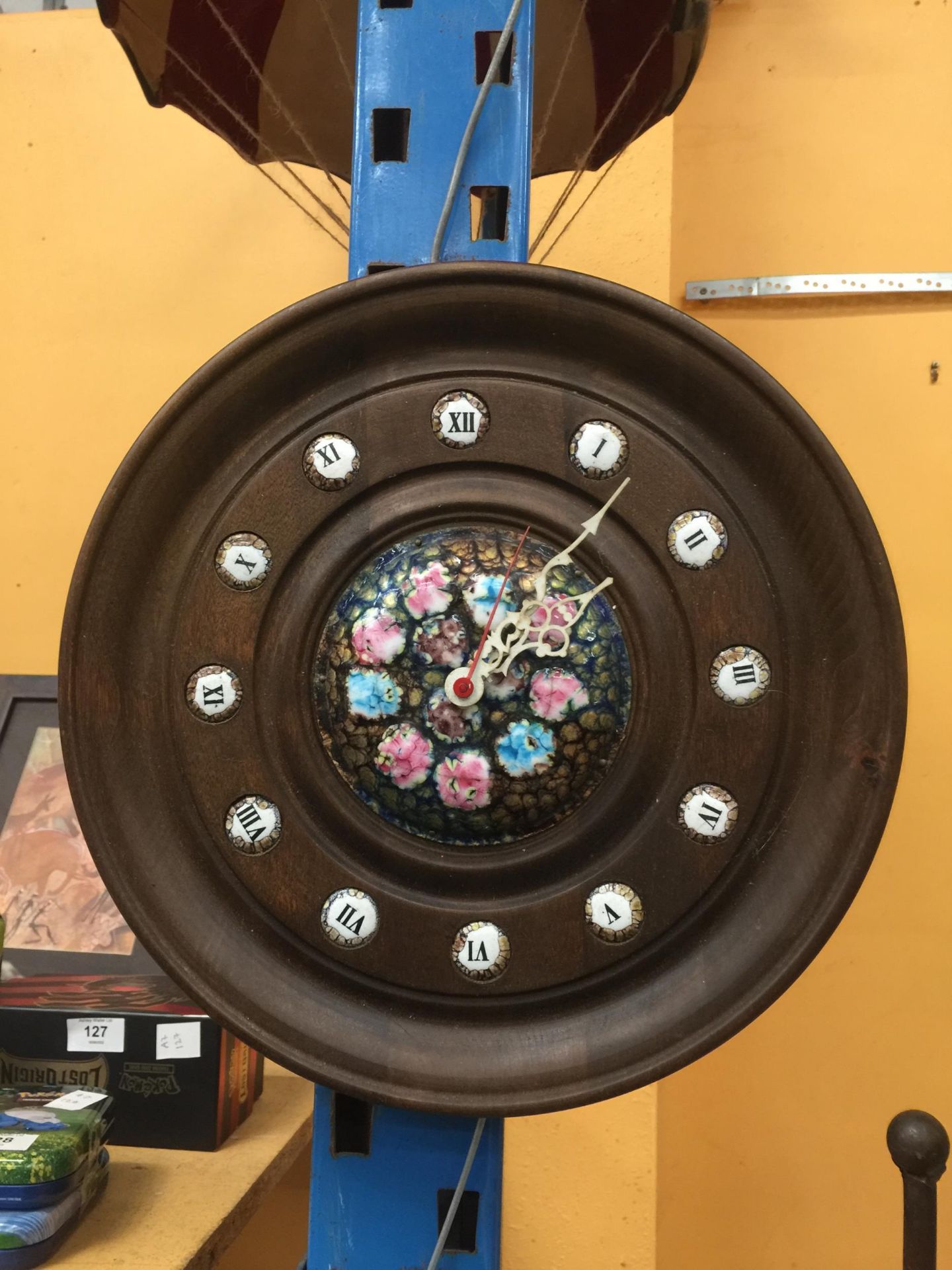A CIRCULAR WOODEN WALL CLOCK WITH ENAMEL HOUR MARKERS AND COLOURED ENAMELLED DIAL
