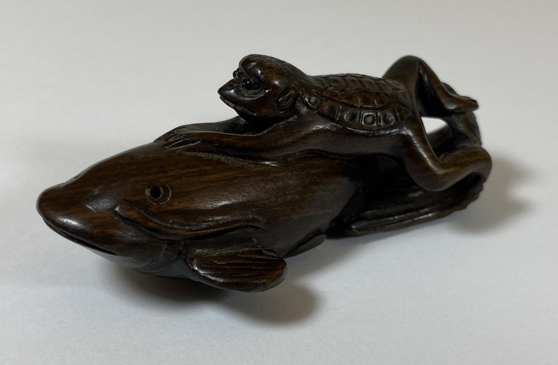 AN ORIENTAL NETSUKE OF A TURTLE MONKEY RIDING A NAMAZU (EARTHQUAKE FISH) SIGNED TO BASE, LENGTH 6.