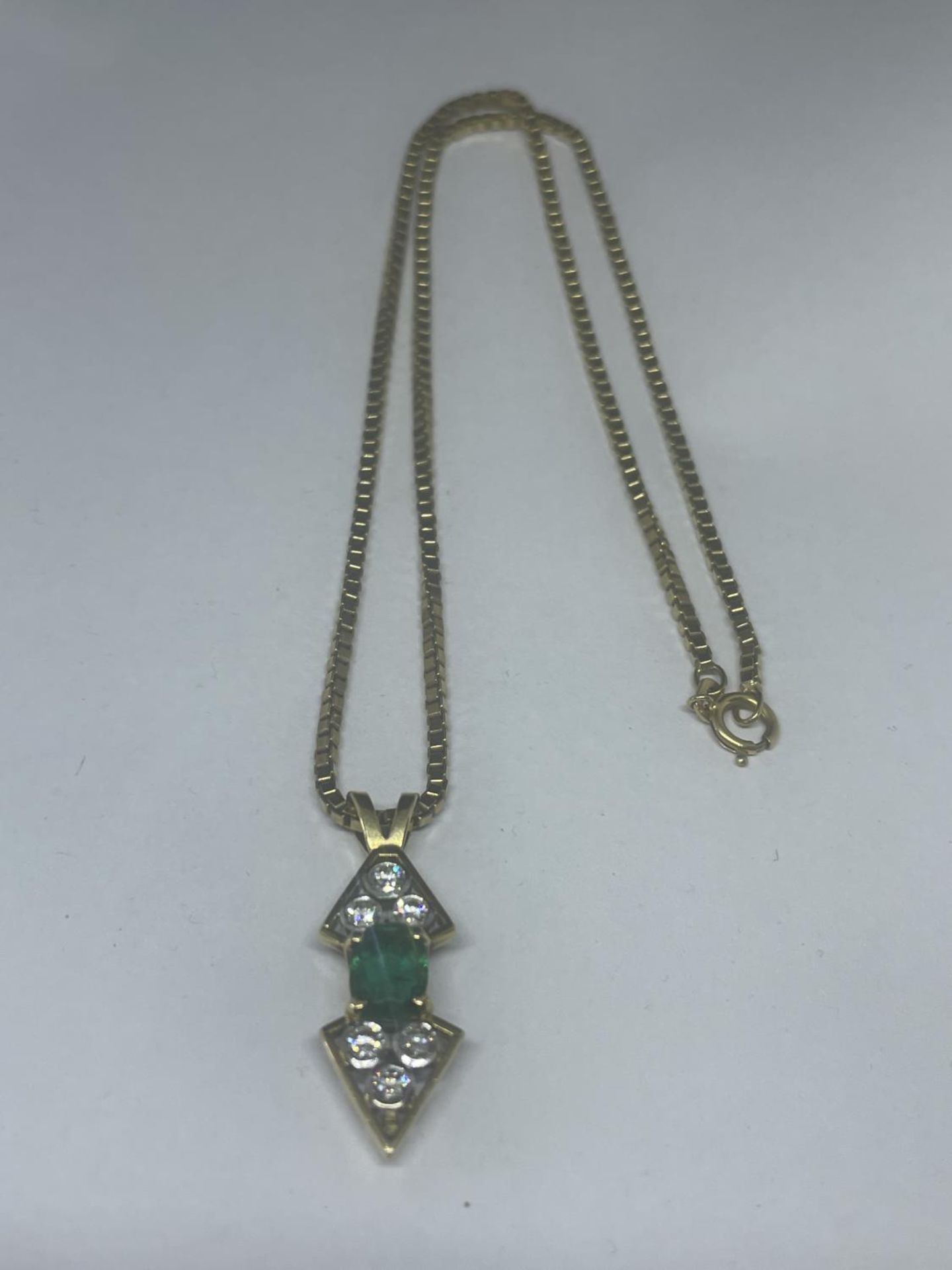 AN 18 CARAT YELLOW GOLD ABSTRACT DESIGN PENDANT WITH CENTRE EMERALD SURROUNDED BY SIX DIAMONDS ON