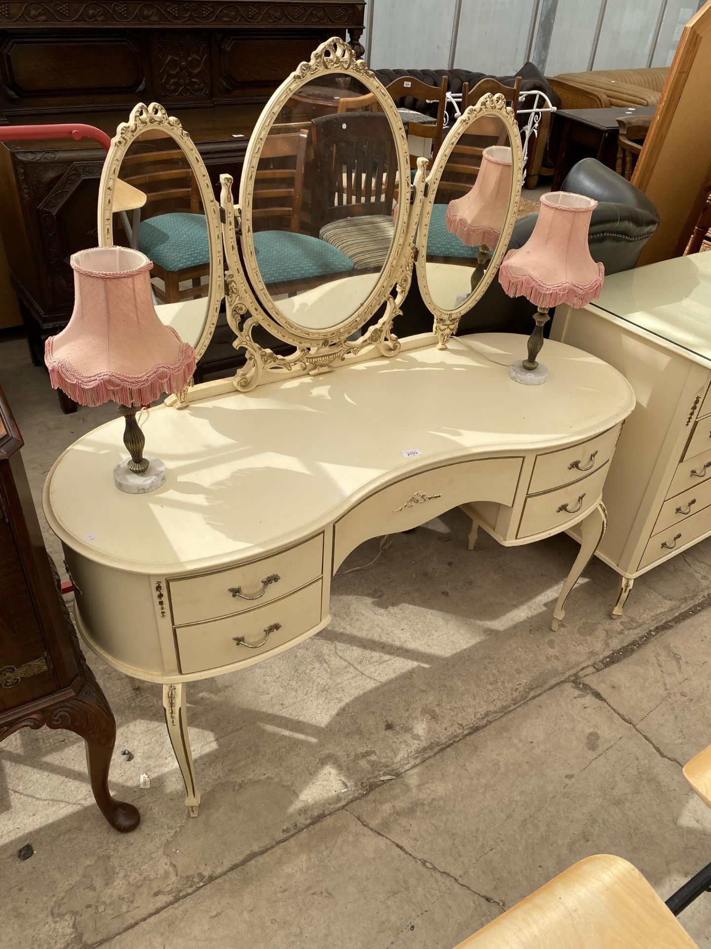 A CREAM AND GILT KIDNEY SHAPED DRESSING TABLE WITH TRIPLE MIRROR AND PAIR OF LAMPS COMPLETE WITH