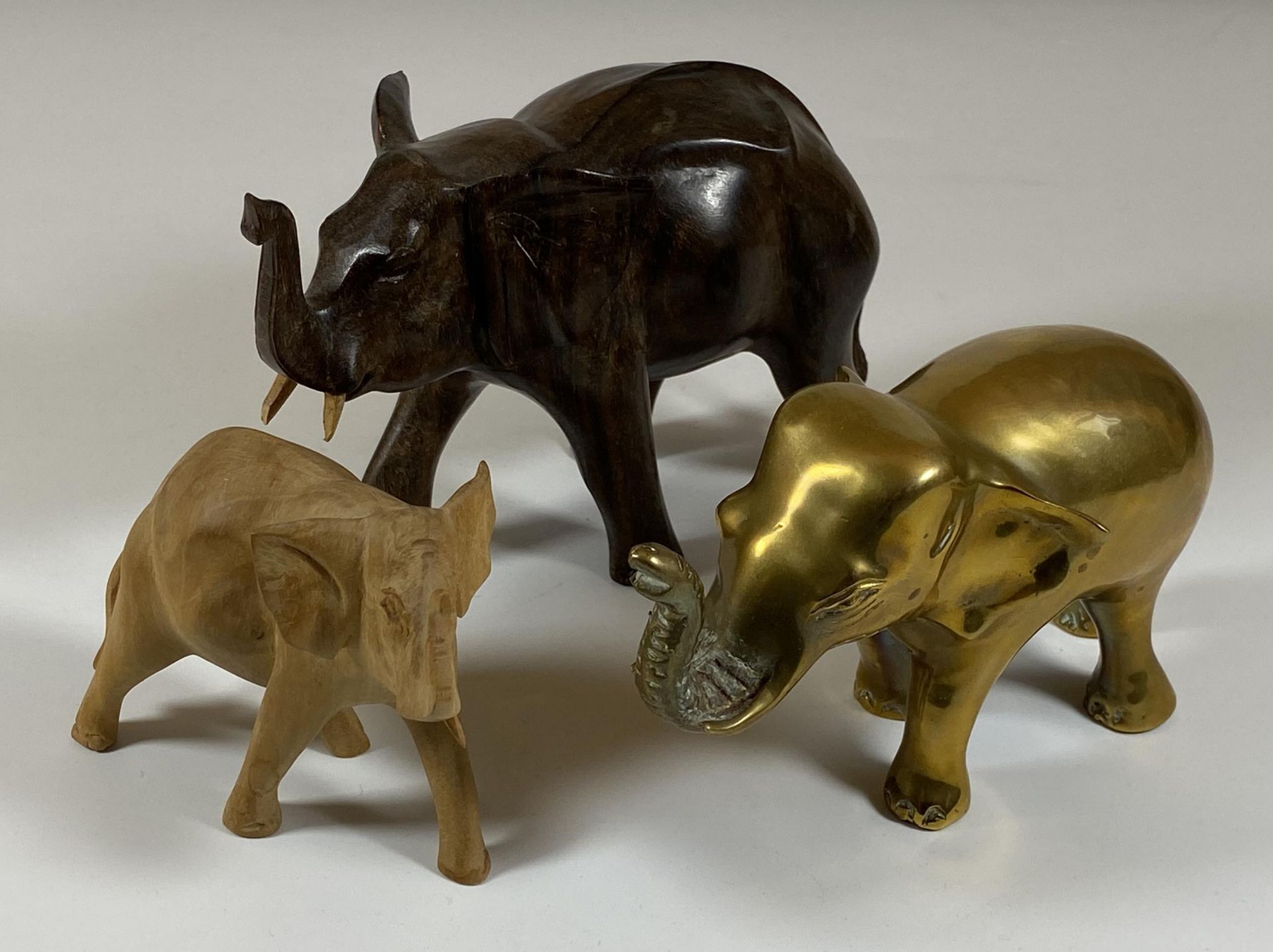 A GROUP OF THREE ELEPHANT FIGURES TO INCLUDE TWO CARVED WOODEN AND A SOLID HEAVY BRASS EXAMPLE,