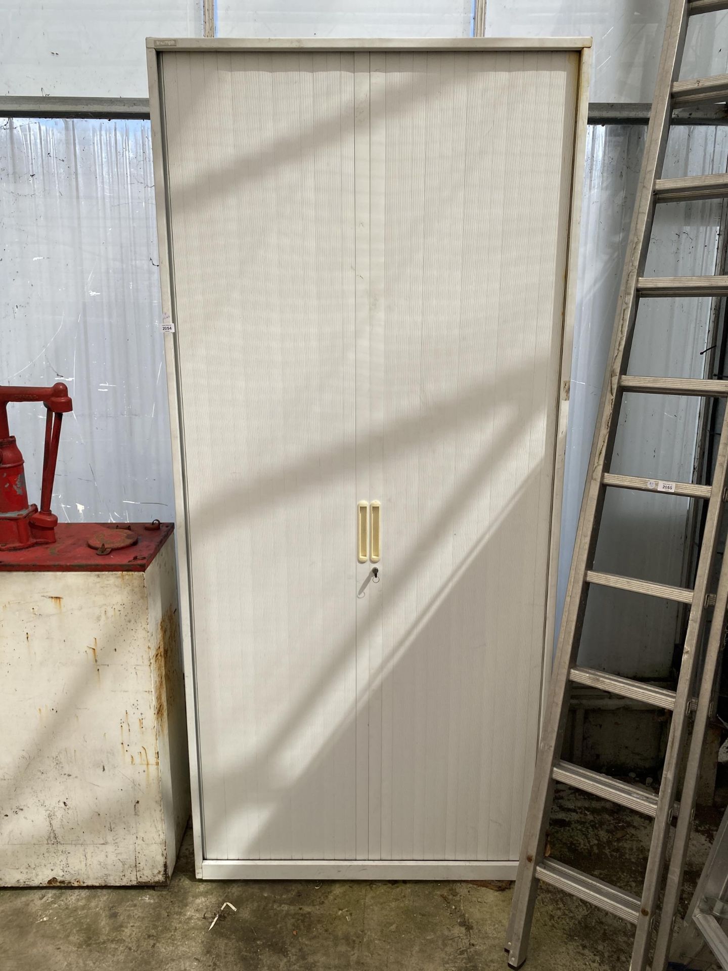 A WHITE METAL STORAGE CABINET WITH A TAMBOURED DOOR AND KEY