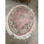 AN OVAL SALMON PATTERNED FRINGED RUG