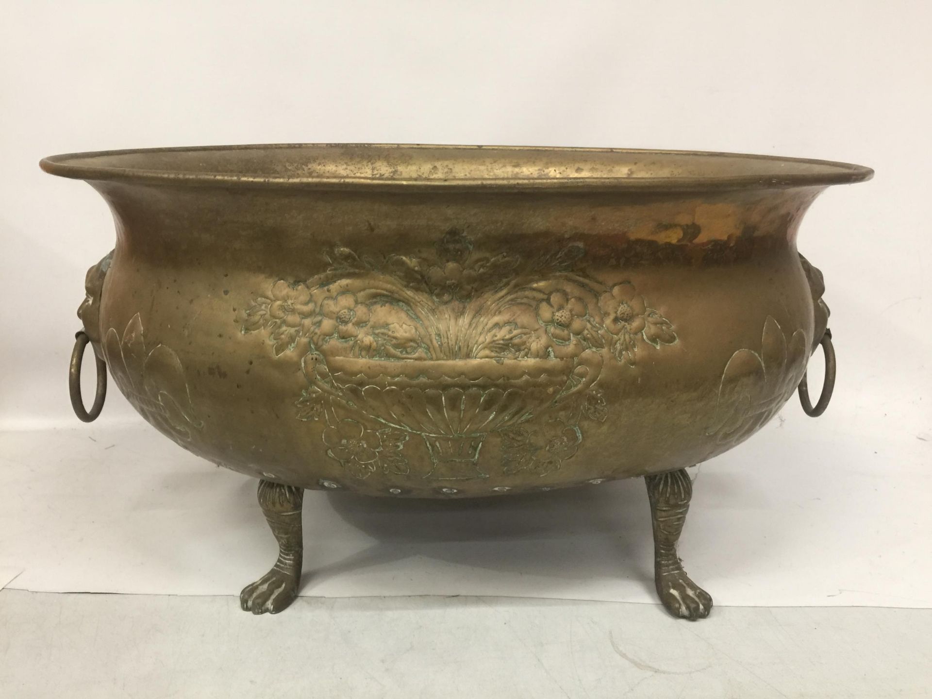 A LARGE BRASS BOWL ON PAW FEET WITH FIGURAL HANDLES