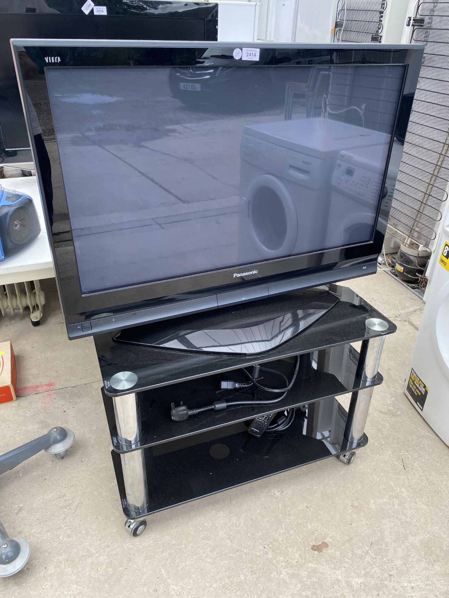 A PANASONIC TELEVISION WITH GLASS TV STAND, CABLE AND REMOTES