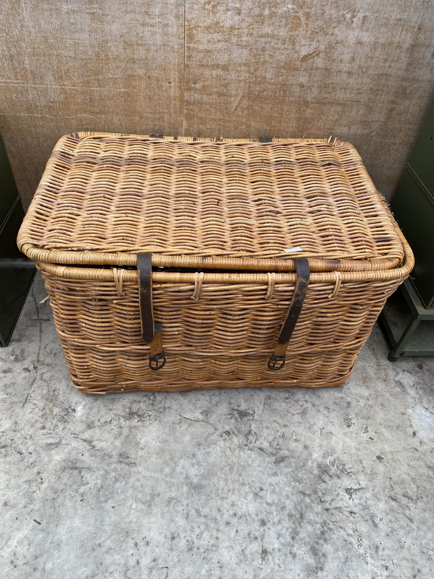 A LARGE WICKER LOG BASKET WITH HINGED LID AND LEATHER STRAPPING
