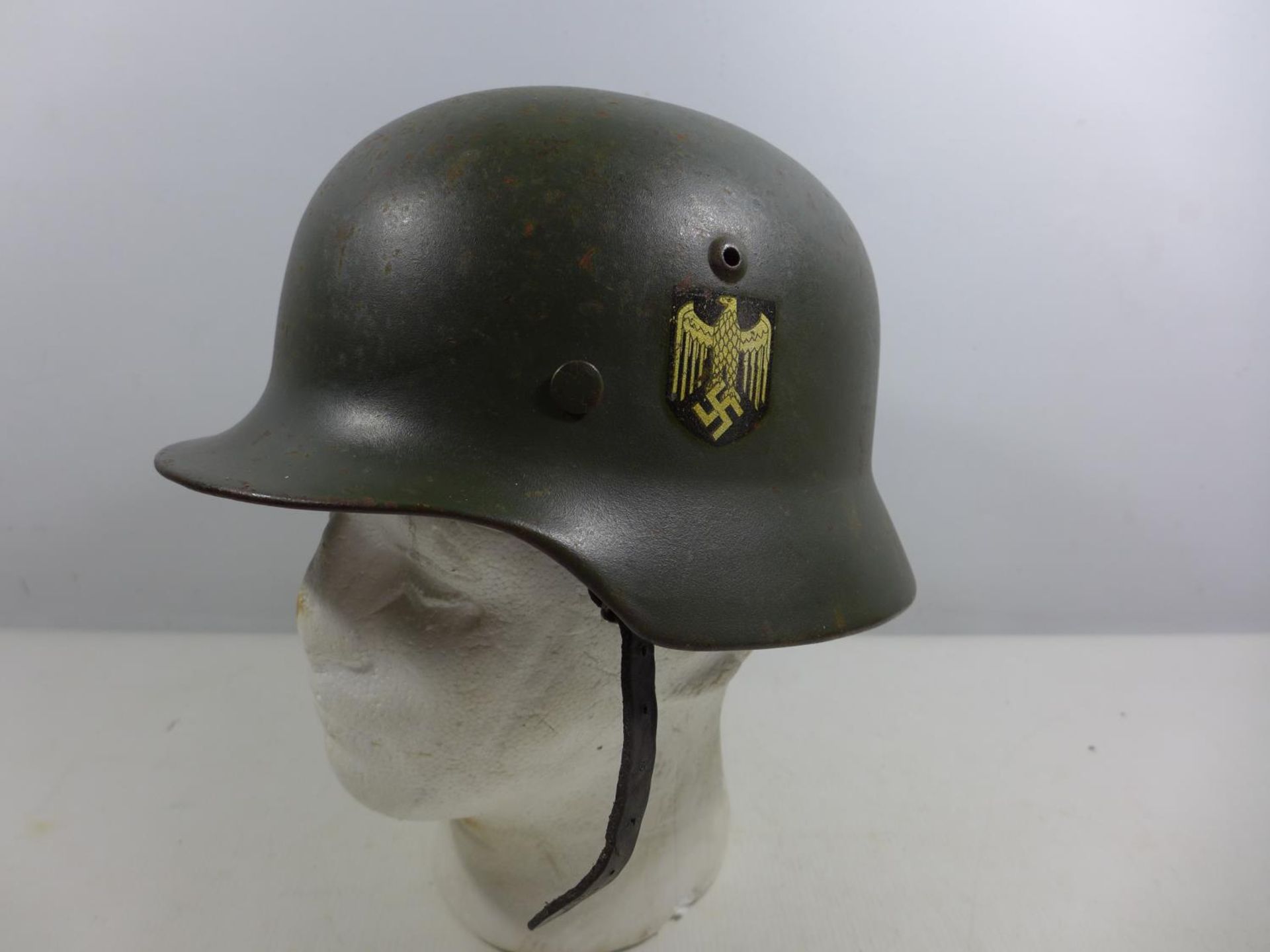 A GERMAN GREEN PAINTED METAL HELMET WITH EAGLE AND SWASTIKA DECORATION AND LEATHER LINING