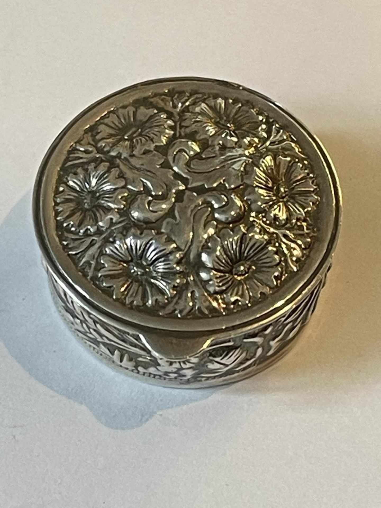 A SILVER CIRCULAR PILL BOX WITH FLORAL DECORATION