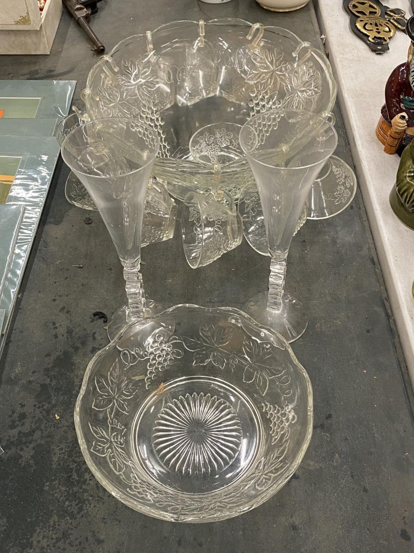A GLASS PUNCH BOWL WITH CUPS DECORATED WITH GRAPES, TWO CHAMPAGNE FLUTES, ETC