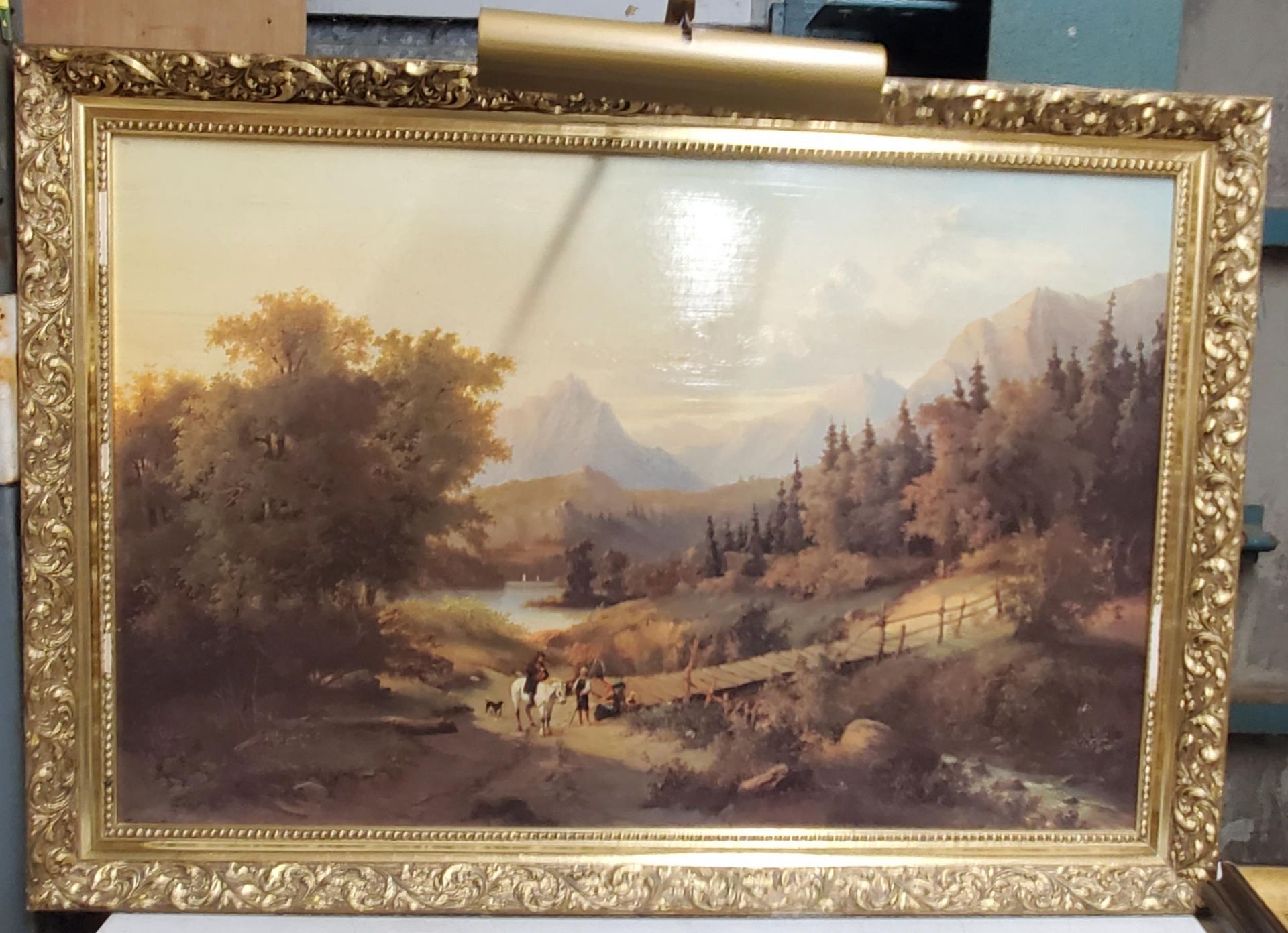 A LARGE PRINT OF PEOPLE AT A MOUNTAIN LAKE WITH ORNATE FRAME AND PICTURE LIGHT