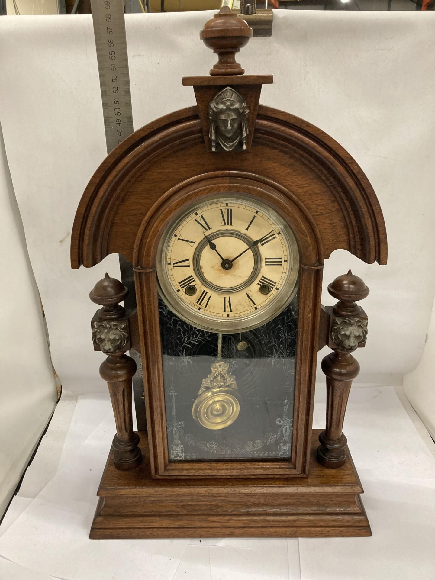 A VINTAGE OAK CHIMING MANTLE CLOCK WITH COLUMN SUPPORTS HAVING LION HEAD DESIGN, WITH PENDULUM,