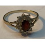 A 9 CARAT GOLD RING WITH A CENTRE GARNET SURROUNDED BY CUBIC ZIRCONIAS SIZE O/P