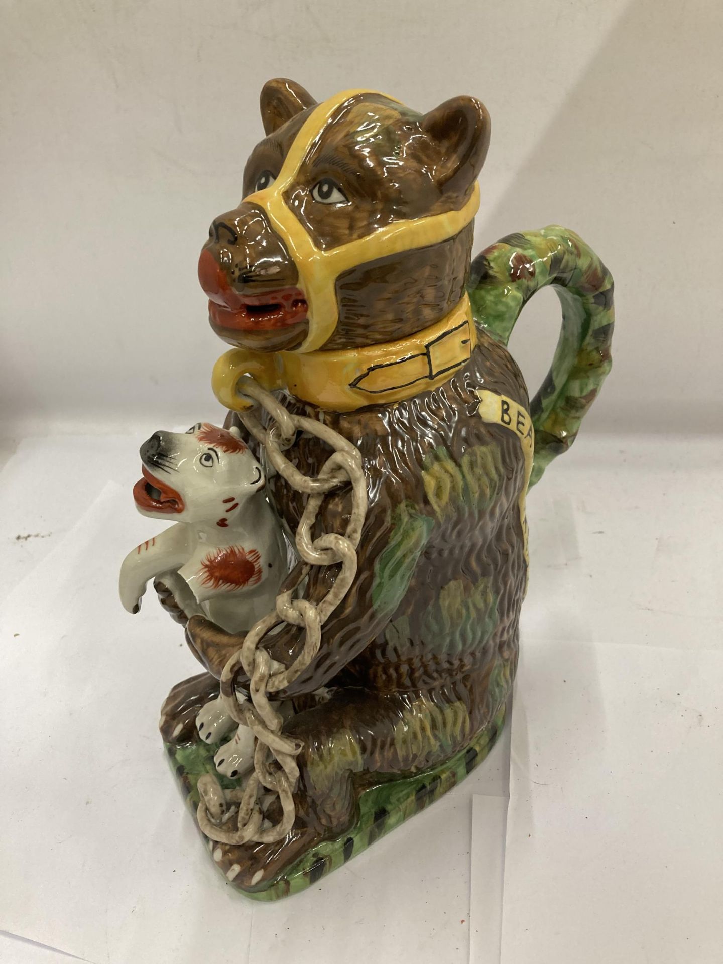 A MAJOLICA STYLE BEAR JUG DEPICTING A CHAINED BEAR HOLDING A DOG, DOGS ARM A/F