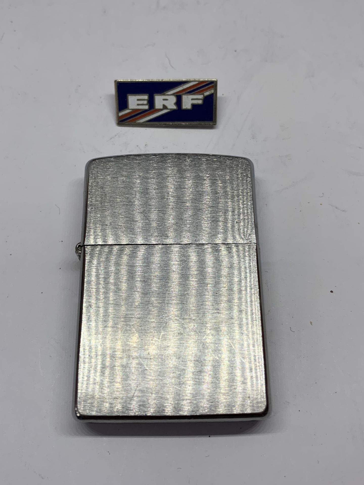 A MADE IN USA ZIPPO LIGHTER AND AN ENAMEL ERF BADGE