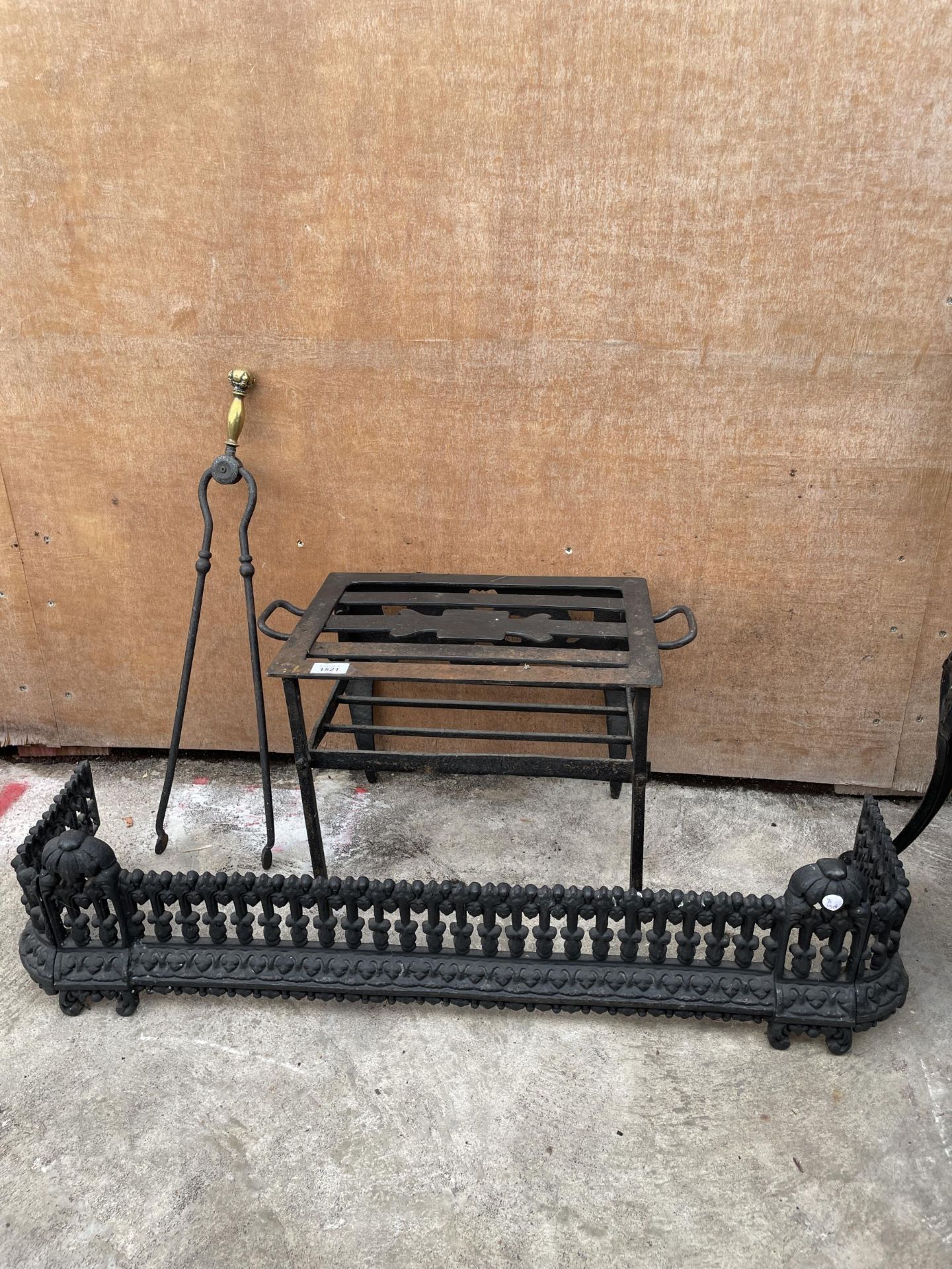 A DECORATIVE CAST IRON FIRE FENDER, A WROUGH IRON TRIVET STAND AND A PAIR OF FIRE TONGS