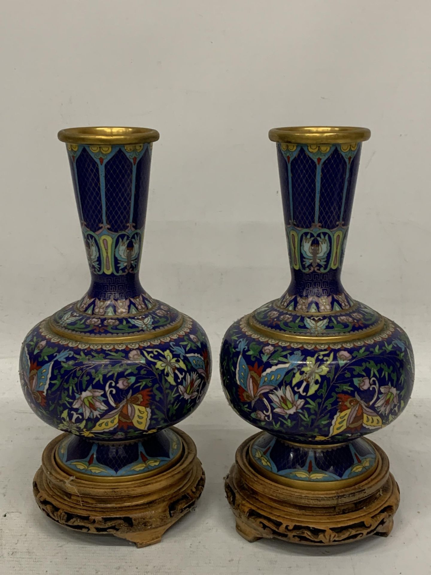 A PAIR OF CHINESE CLOISONNE VASES WITH BUTTERFLY DECORATION ON CARVED WOODEN STANDS