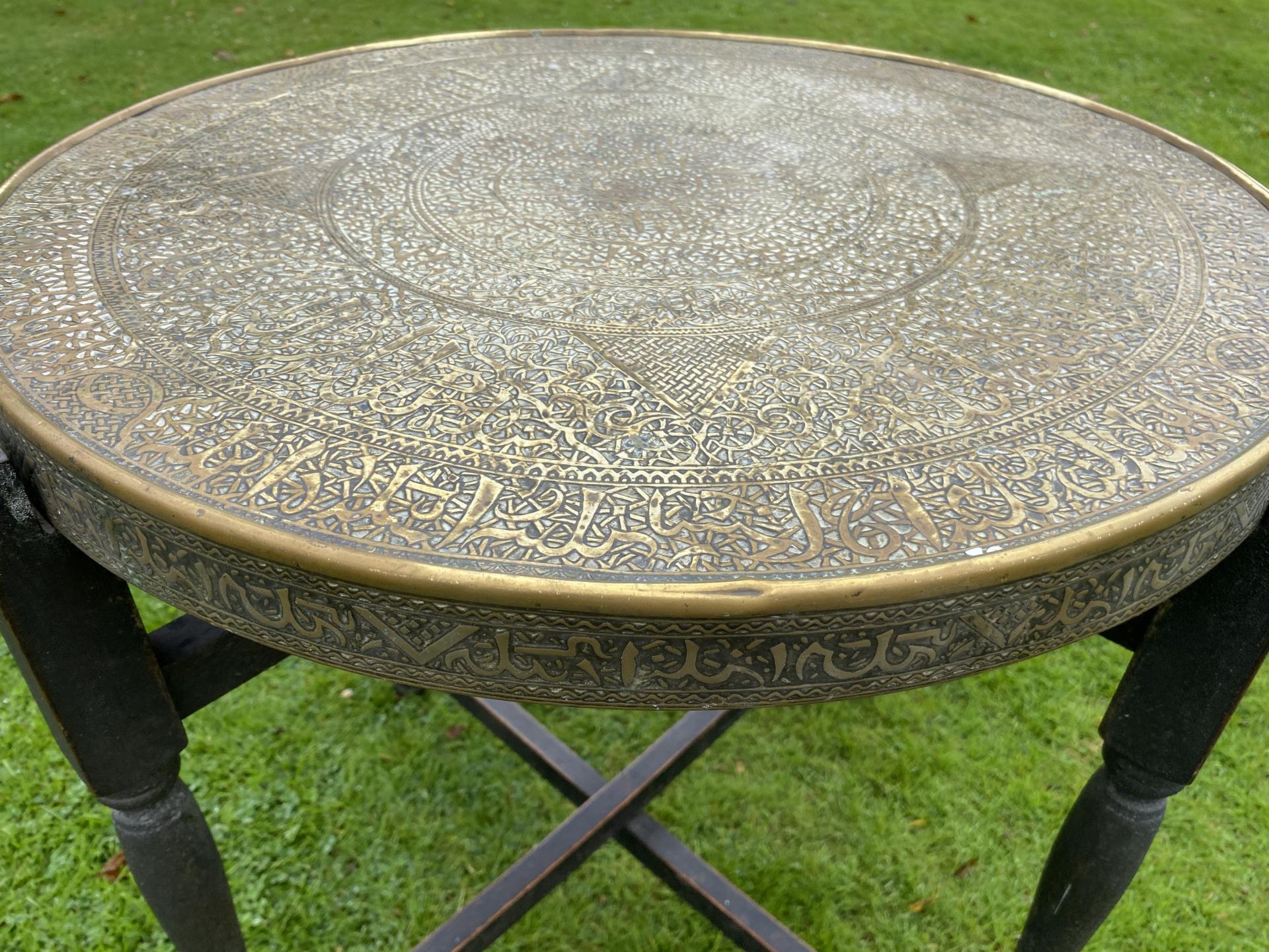 A MIDDLE EASTERN BRASS CIRCULAR TOPPED TABLE ON FOLDING WOODEN BASE, DIAMETER 59CM - Image 2 of 4