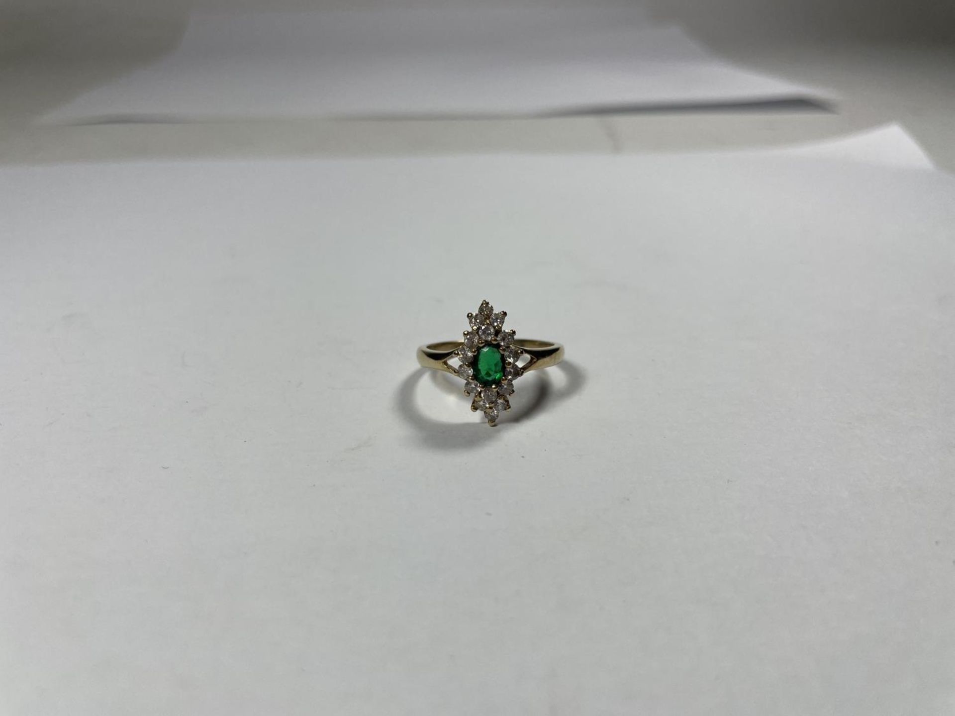 A 9 CARAT GOLD RING WITH CENTRE GREEN STONE SURROUNDED BY CUBIC ZIRCONIAS IN A DIAMOND SHAPE SIZE