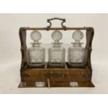 A VINTAGE OAK THREE BOTTLE TANTALUS WITH METAL HANDLE AND MOUNTS WITH LOCKABLE FALL FRONT (ONE