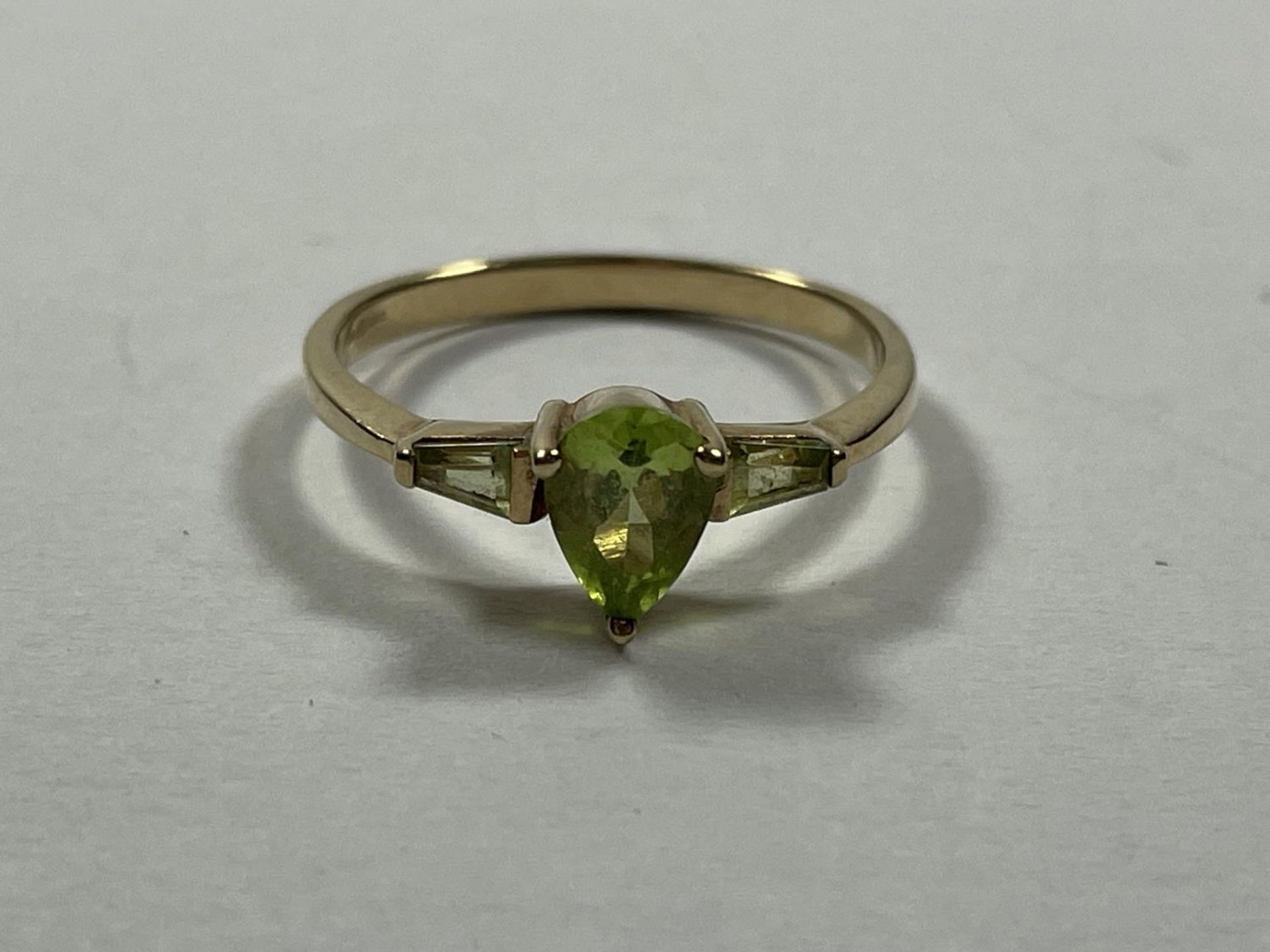 A 9 CARAT GOLD RING WITH A TEARDROP PERIDOT STONE AND ONE TO EACH SHOULDER SIZE P