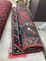 A SMALL RED PATTERNED FRINGED CARPET RUNNER