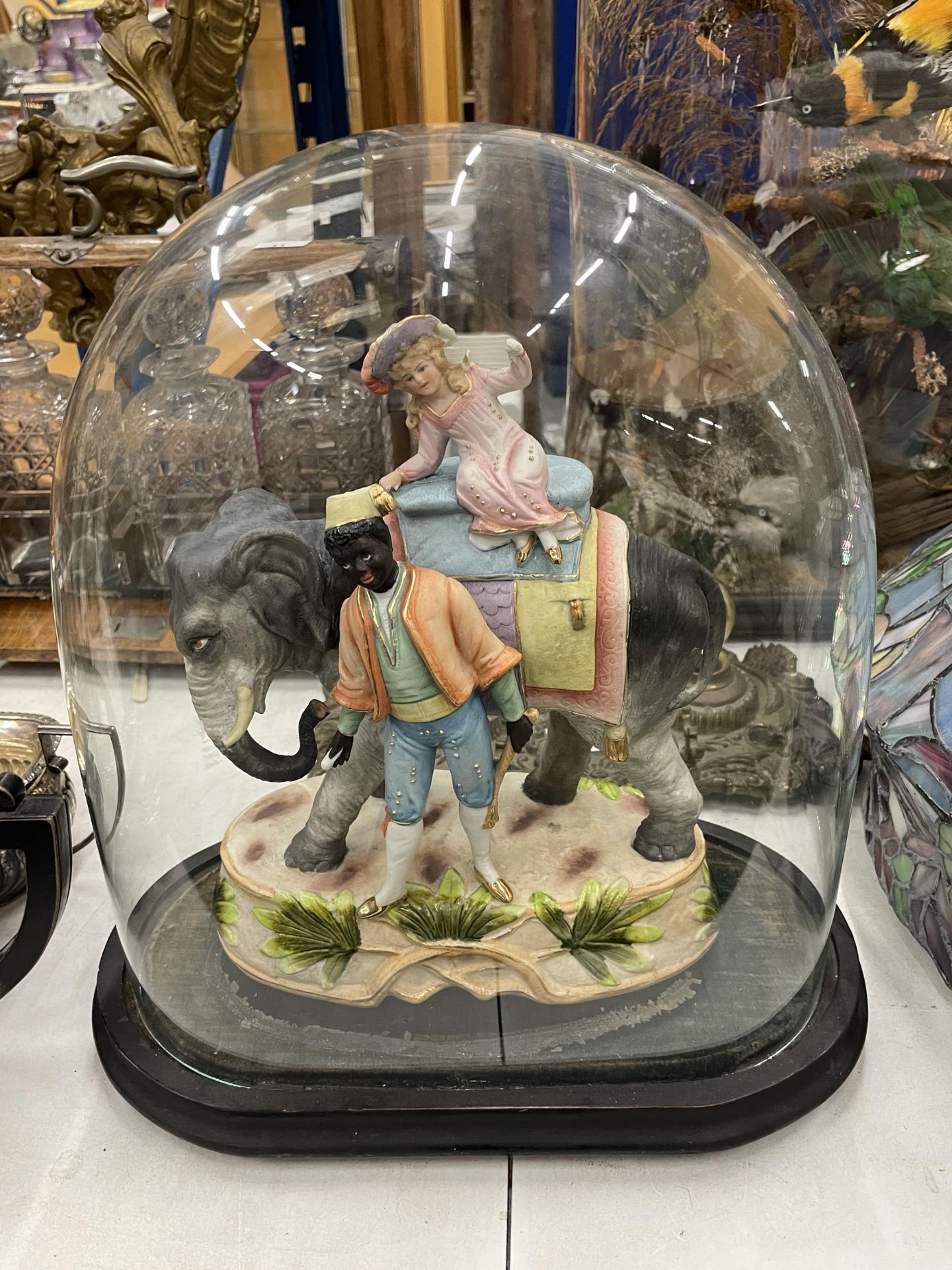 A CONTINENTAL BISQUE FIGURE OF A BOY AND GIRL ON AN ELEPHANT, IN VINTAGE GLASS DOME DISPLAY