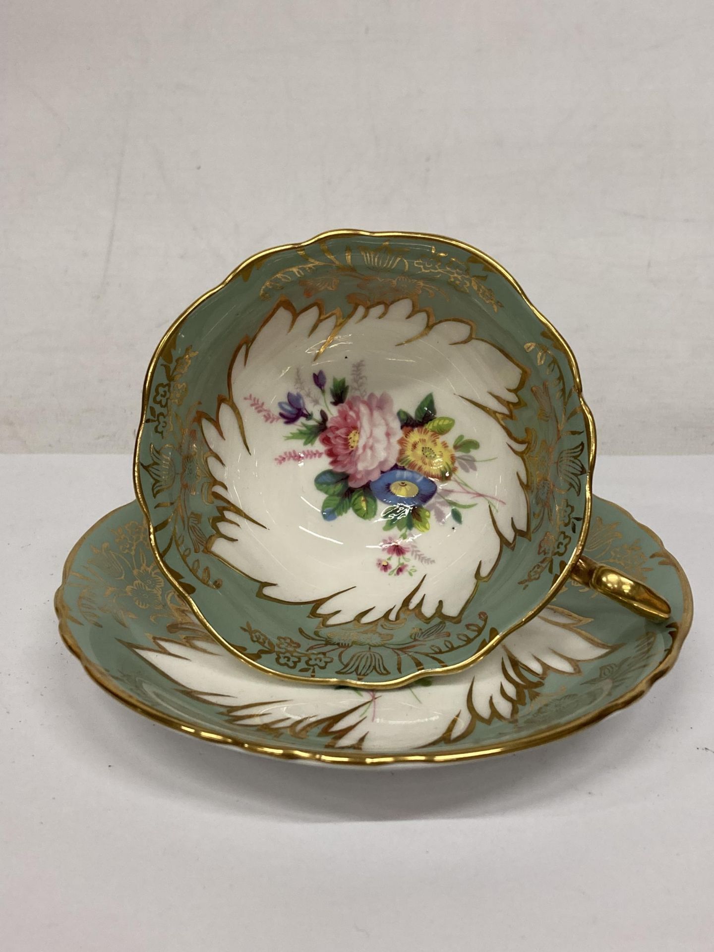 A PARAGON FOOTED TEACUP AND SAUCER GREEN WITH GOLD GILT AND FLORAL SPRAYS